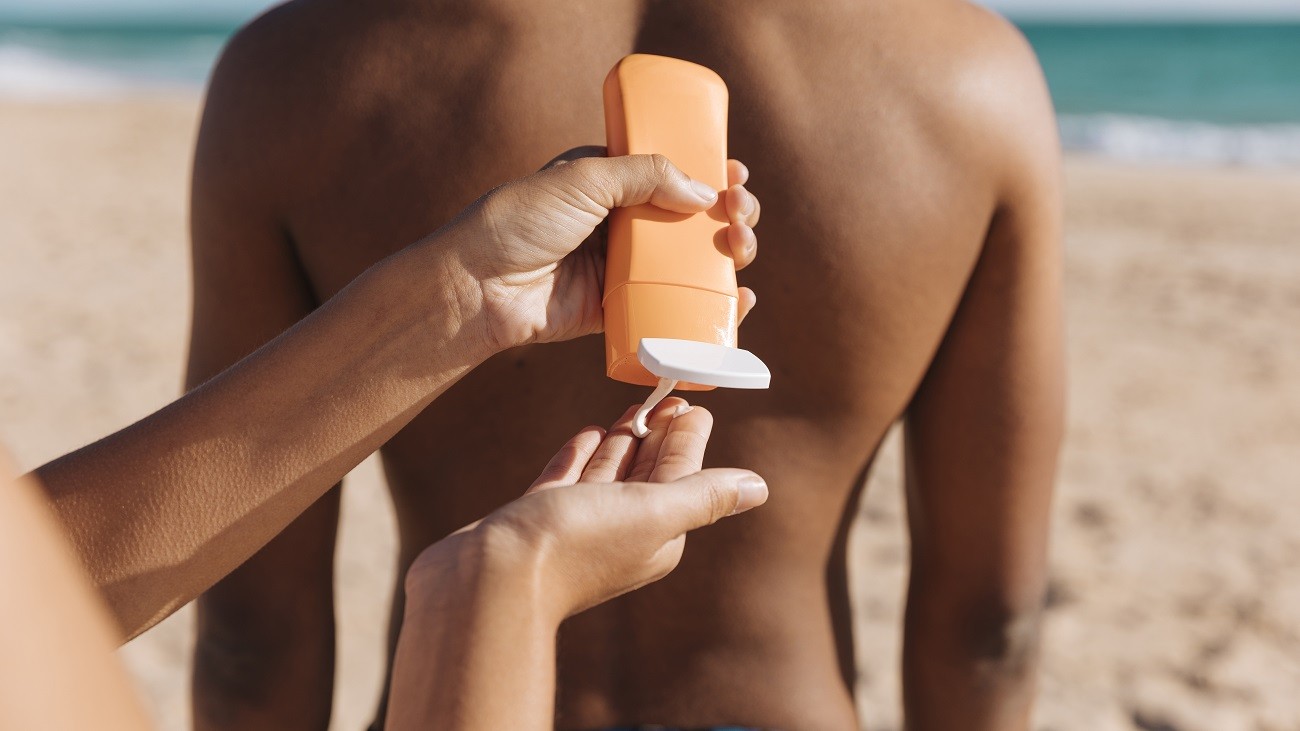 Mãos femininas aplicando protetor solar em um homem, na beira da praia.