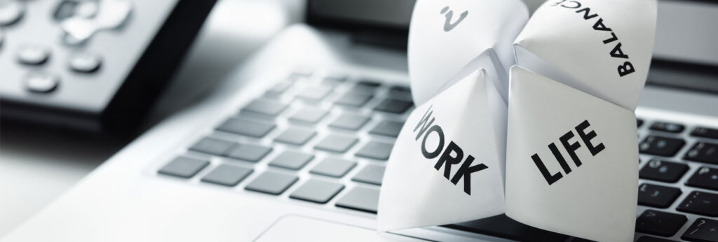 brinquedo de papel com as palavras work, balance e life sobre notebook brinca com a dificuldade de equilibrar vida pessoal e profissional