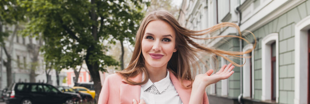 mulher loira com mais de 30 anos caminha na calçada sorrindo e atira os cabelos para trás com autoconfiança e bem-estar