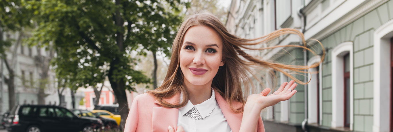 mulher loira com mais de 30 anos caminha na calçada sorrindo e atira os cabelos para trás com autoconfiança e bem-estar
