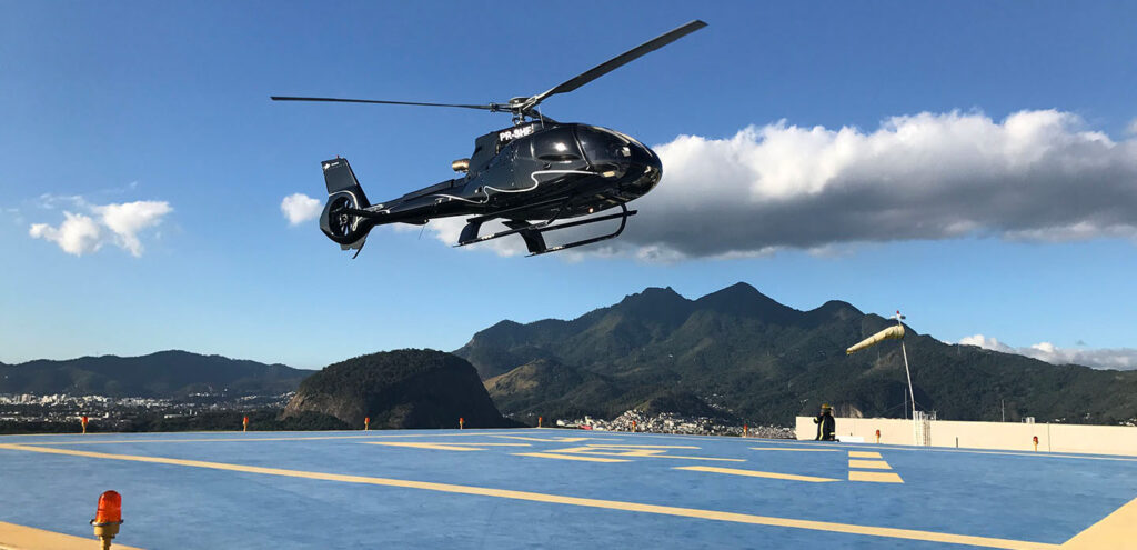helicoptero pousa em heliponto no fundo céu zul com nuvem e montanhas